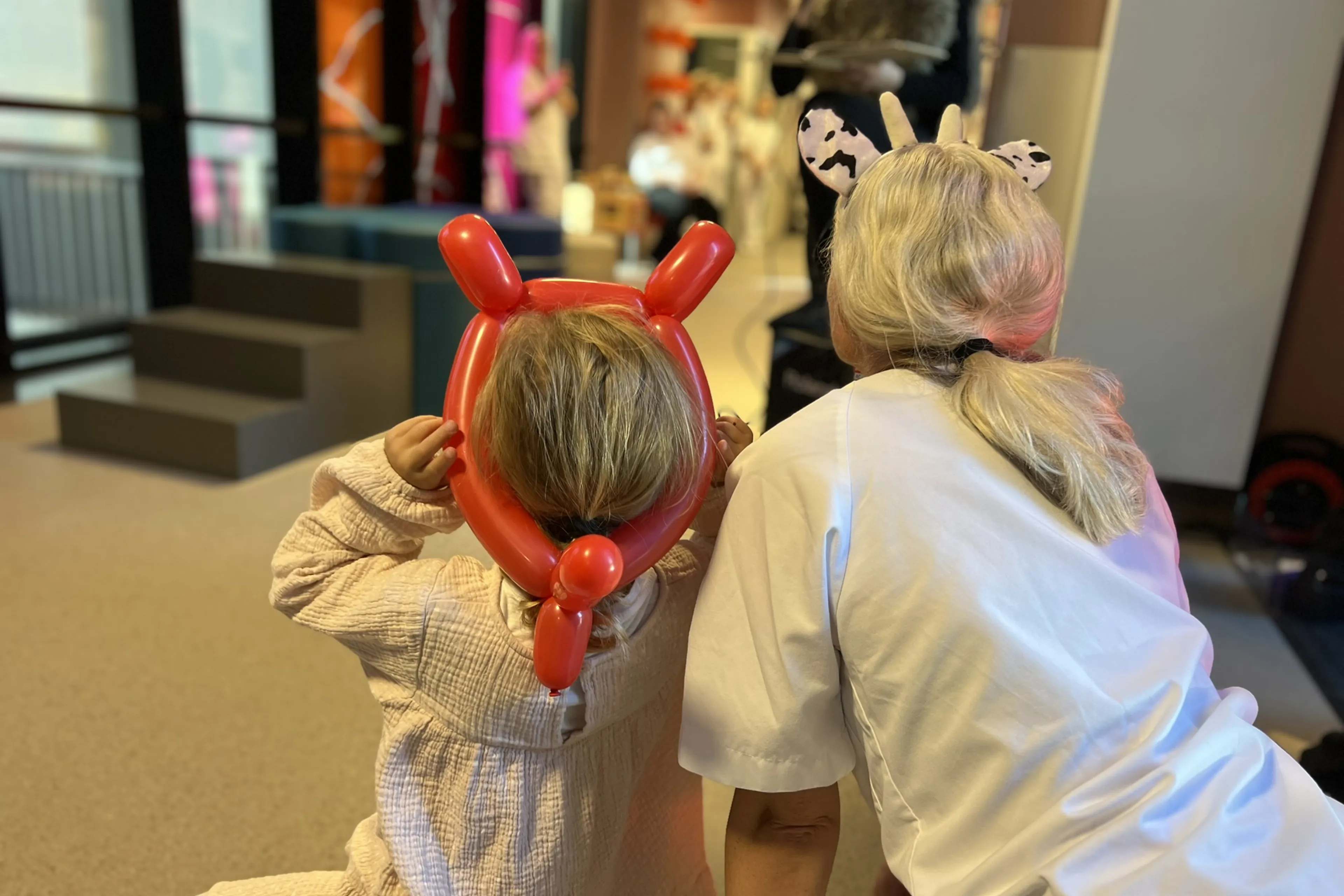 Eit barn med ballonghorn på hovudet, og ein sjukepleiar som føl med på ei eventyrfortelling