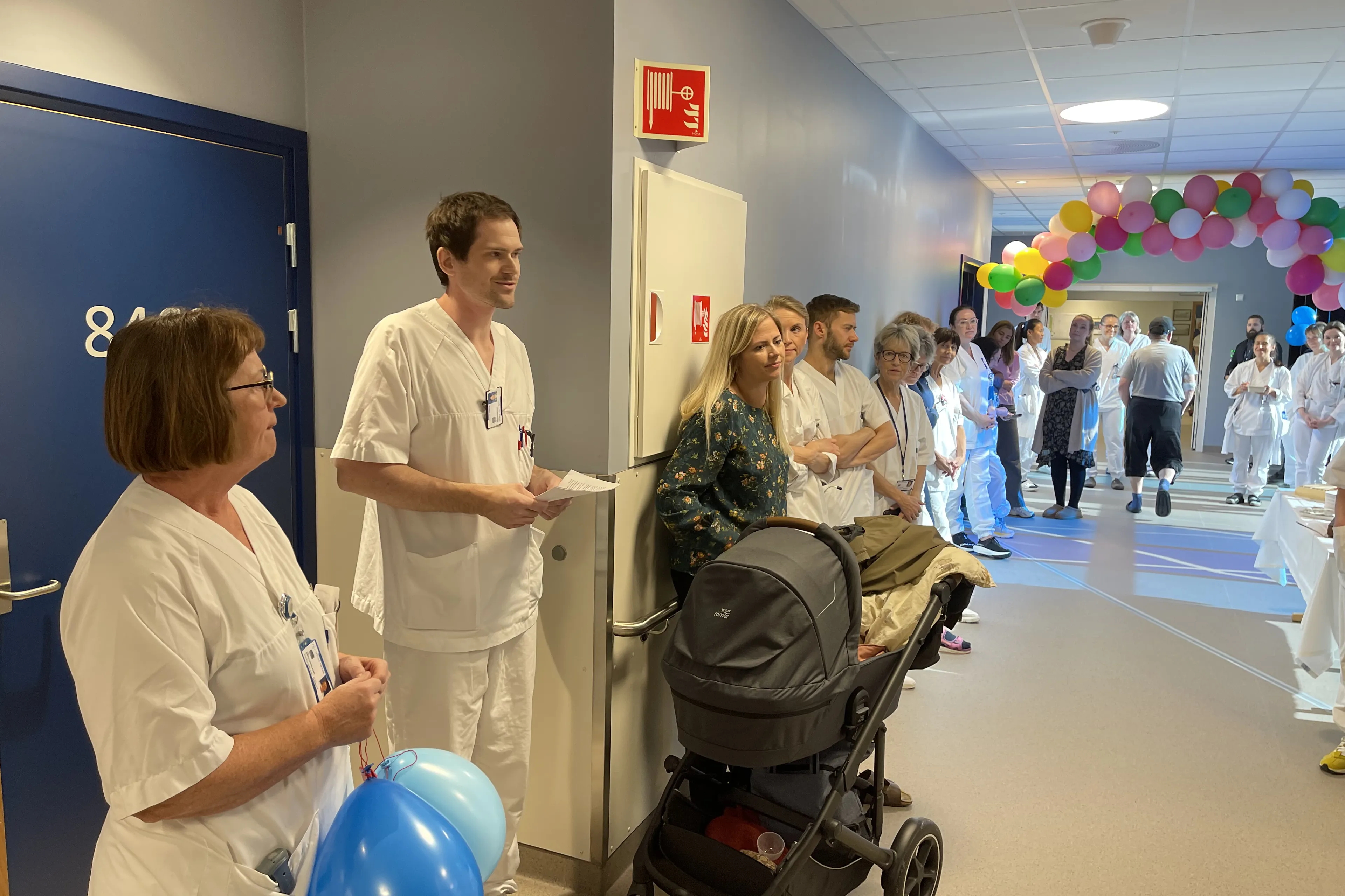 Ei gruppe personar i kvite helsepersonelluniformar i eit rom med ballongar