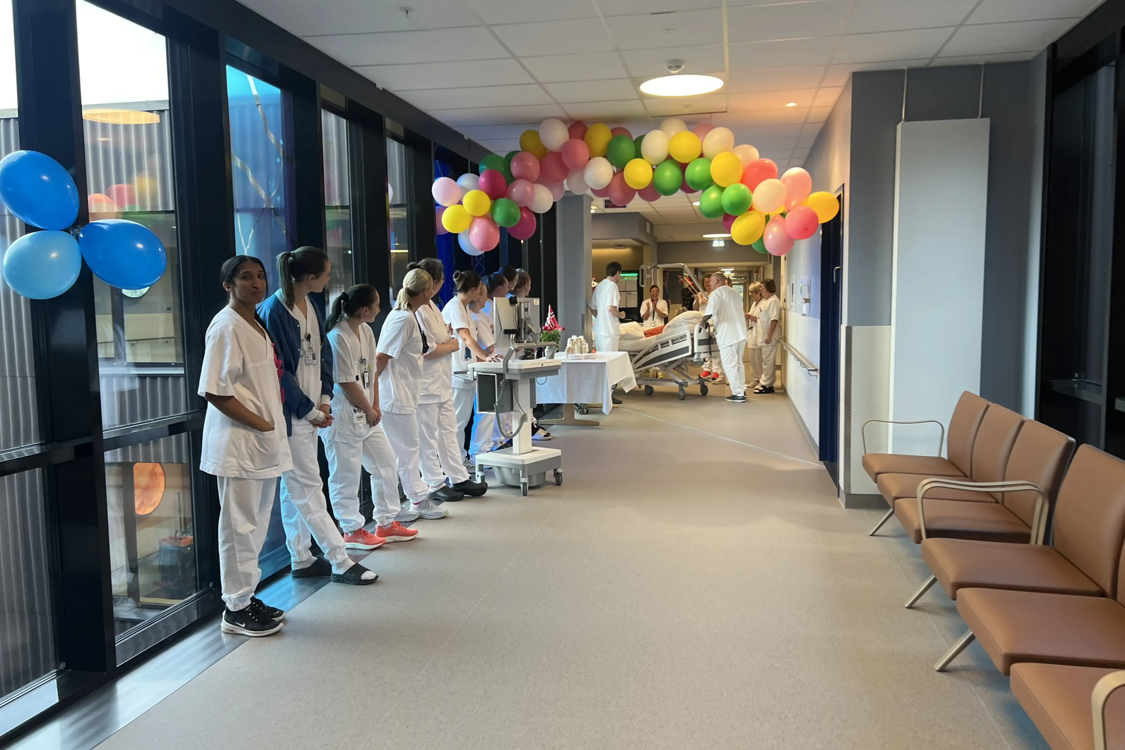 Ei gruppe tilsette i kvite uniformar som står i ein gang med ballongar, mens den første pasienten blir trilla inn i Livabygget.