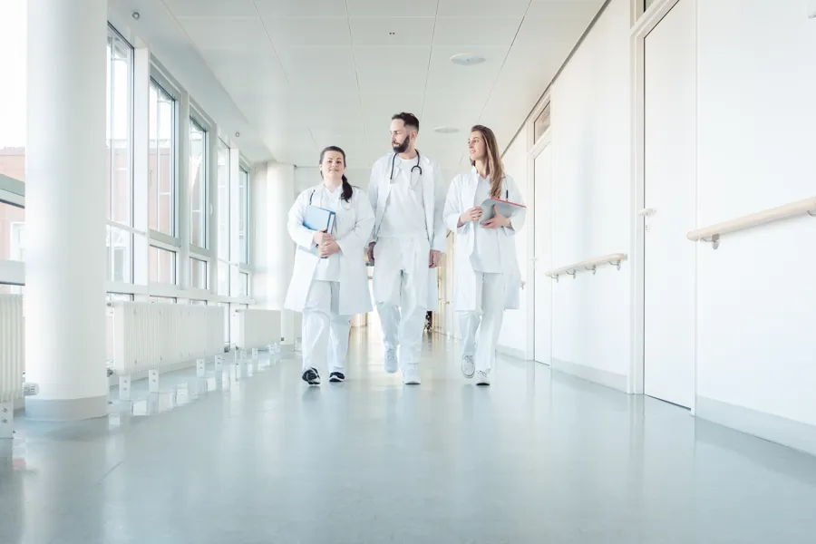 tre legestudentar i kvite frakkar i ein sjukehuskorridor