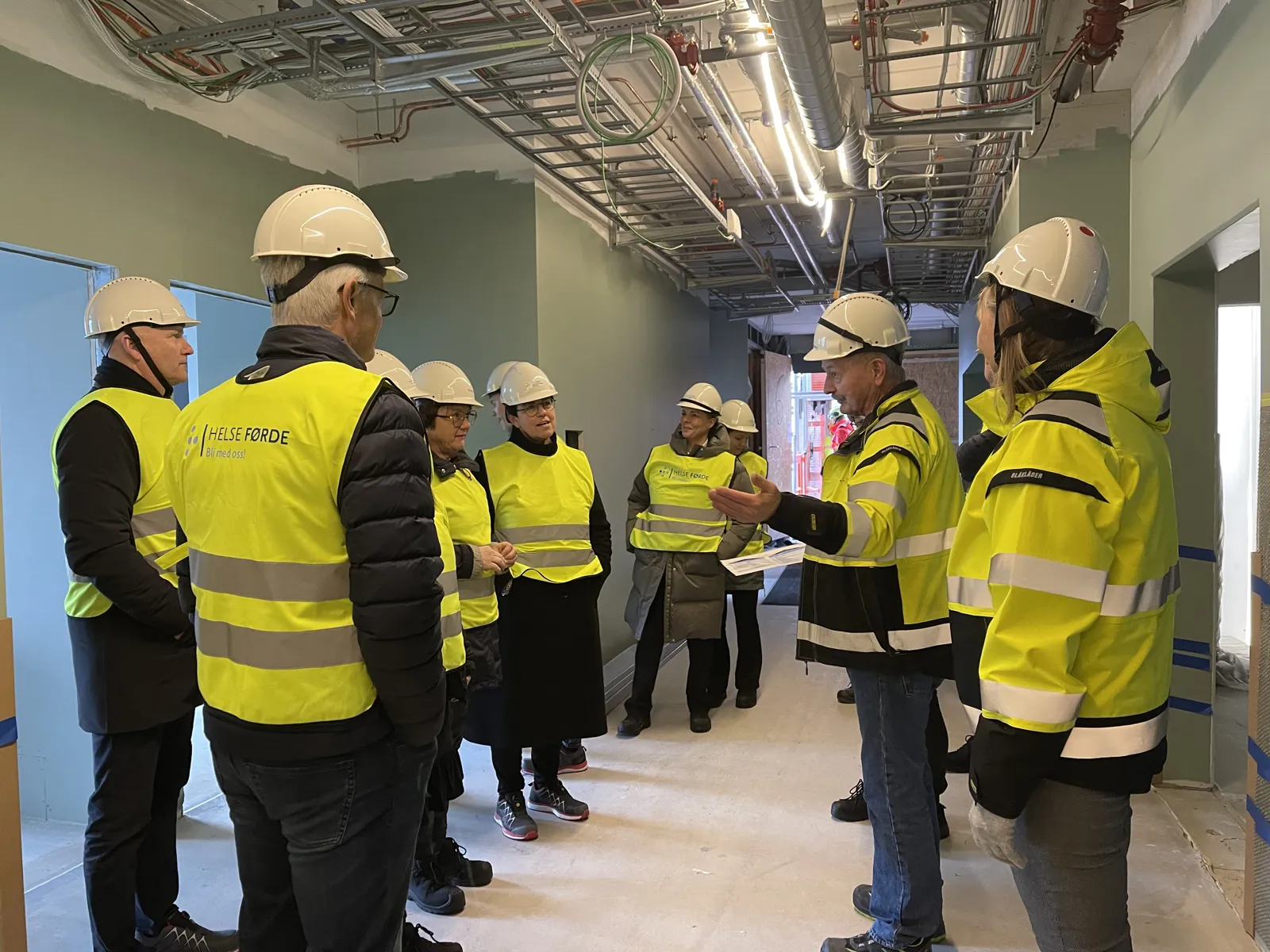 Ei gruppe menneske kledd i sikkerheitvestar på synfaring i eit bygg under oppføring.