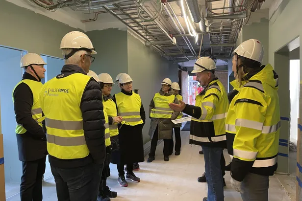Ei gruppe menneske kledd i sikkerheitvestar på synfaring i eit bygg under oppføring.