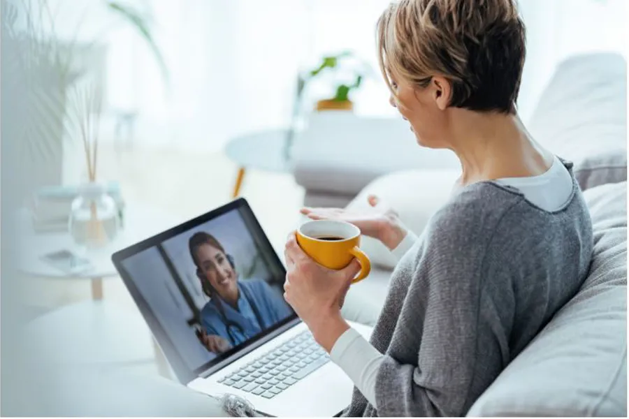 Ei kvinne som sit med ei datamaskin på fanget, og held ein kopp kaffe mens ho har ein videosamtale