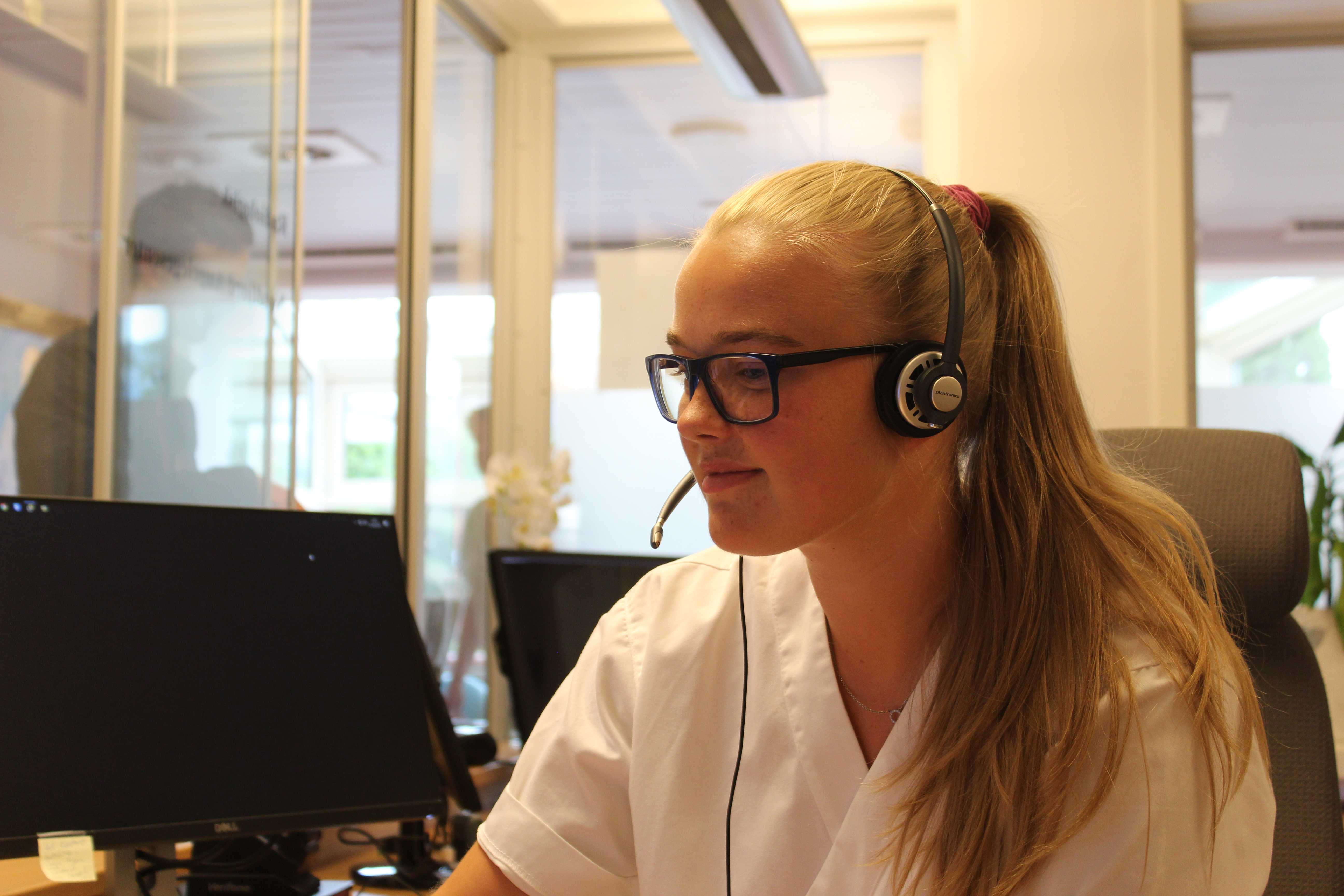 ei ung kvinne ved sentralsbordet som sit framfor ei datamaskin med hovudtelefonar på seg.