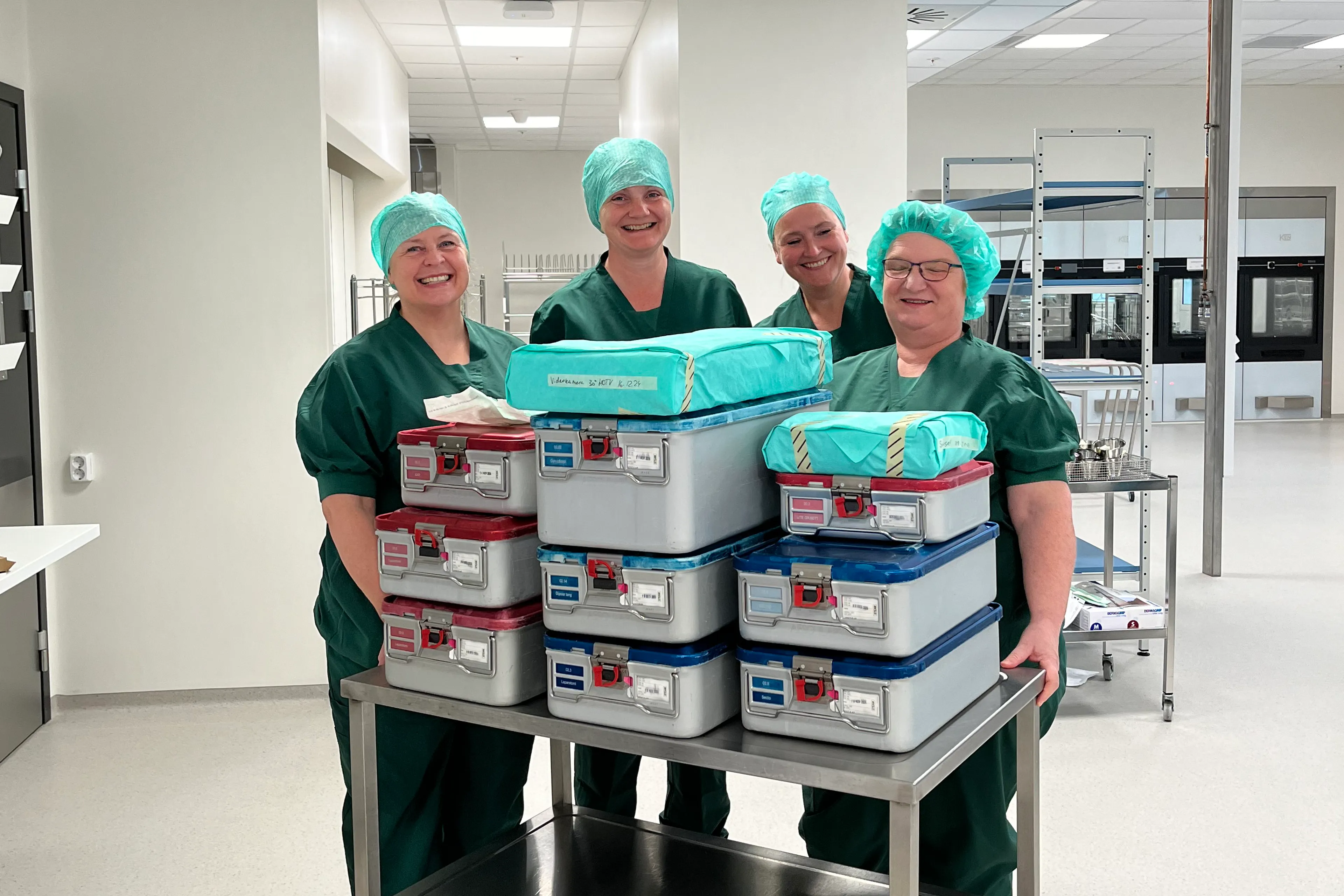 Grønkledde kvinner med hette på hovudet som står framfor ei tralle