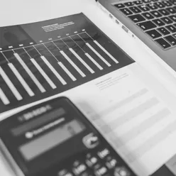 bilete i svart og kvitt som viser litt av ein laptop og eit dokument med søyler og tal