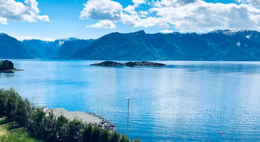 Fjord og fjellandskap som badar i sommarsol