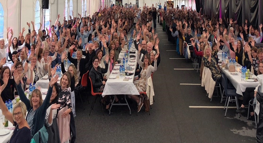 ei stor samling av glade mennesker som sit rundt langbord