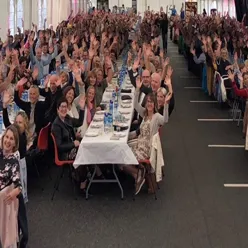 ei stor samling av glade mennesker som sit rundt langbord