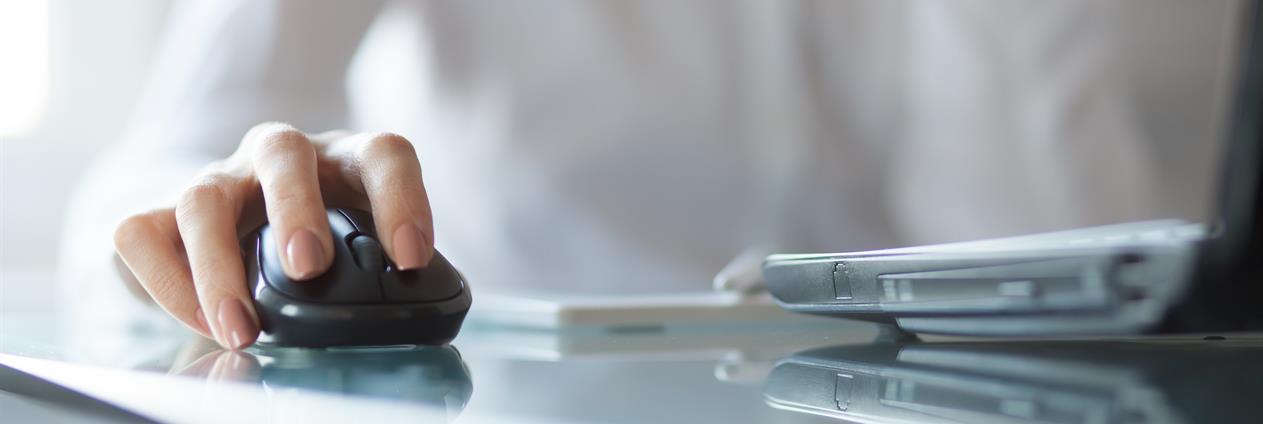 nærbilde av ei kvinnehand som held på ei datamus. Vi skimtar konturane av ein bærbar pc